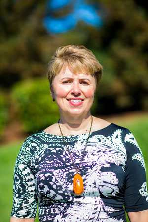 The image shows a woman standing outdoors, smiling at the camera.